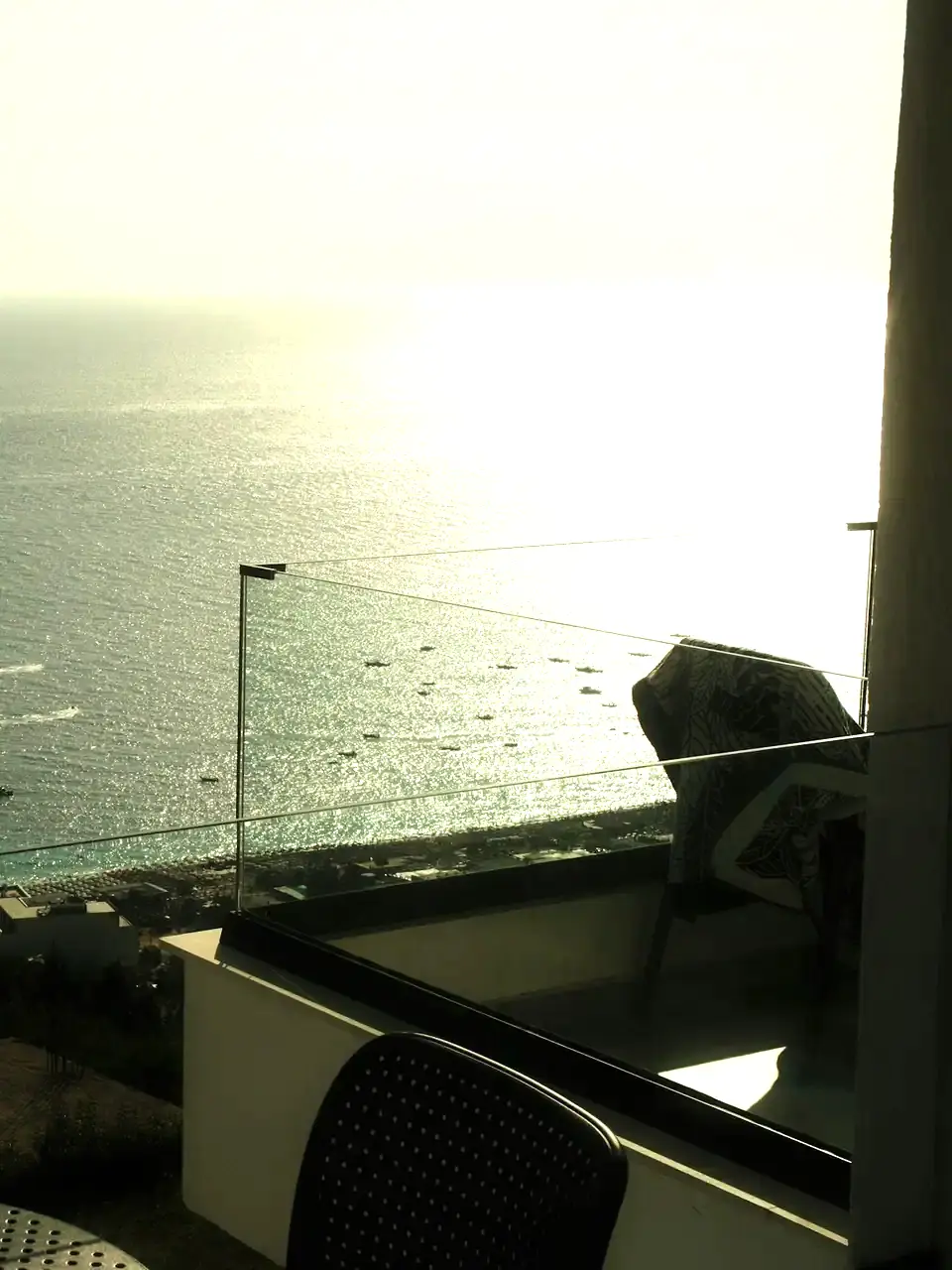 Ocean view at sunset from a balcony with a glass railing